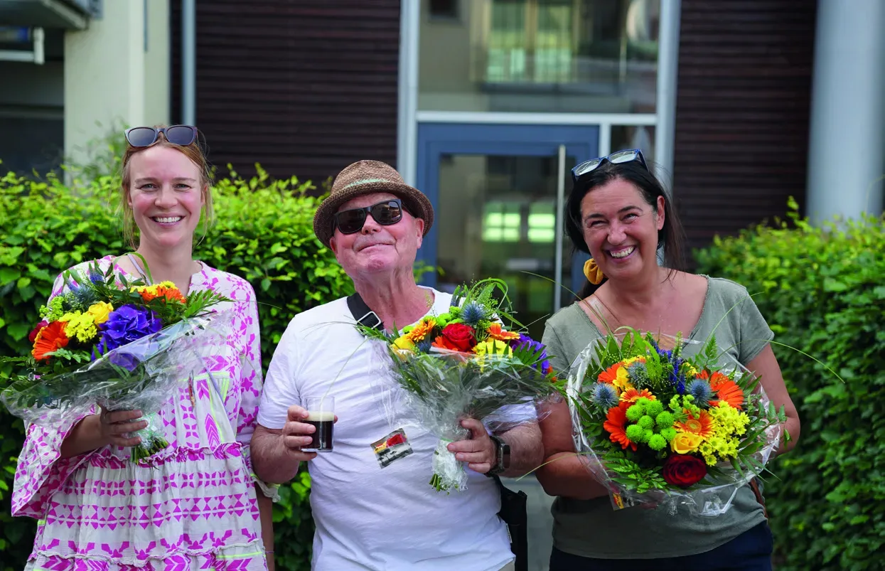 Drei Mitglieder der Arbeitsgemeinschaft mit Blumensträußen
